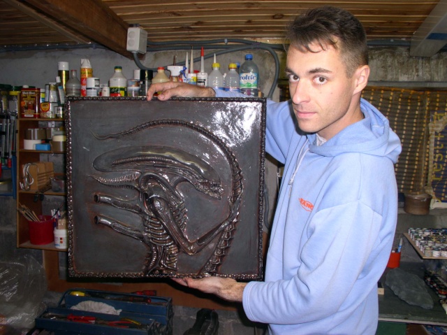 Maquettiste tenant un bas relief patiné représentant la créature Alien dans son atelier