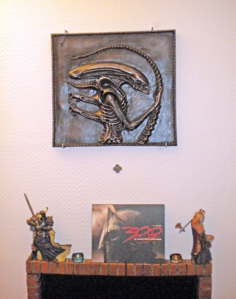 Bas relief patiné de l'Alien accroché au mur au-dessus d'une cheminée décorée de figurines
