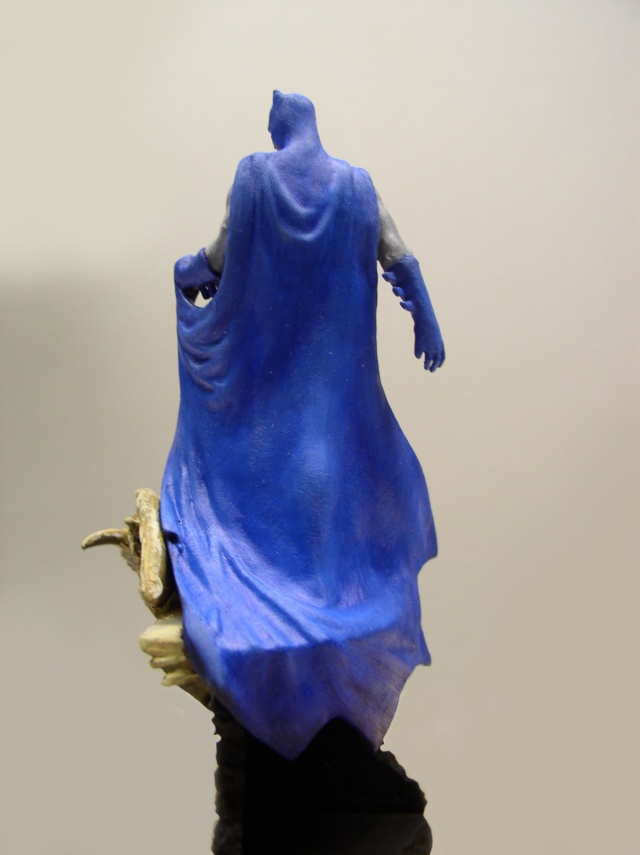Figurine de Batman vue de dos avec cape bleue drapée sur socle rocheux