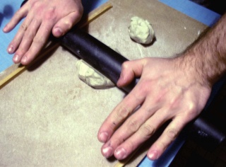 Mains étalant de la pâte à modeler au rouleau pour fabriquer un mur de maquette