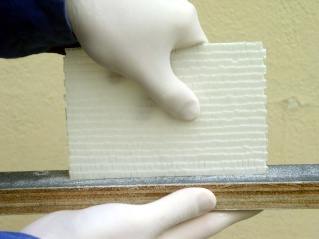 Mains gantées tenant une plaque de carton plume texturée pour la maquette de maison à colombage