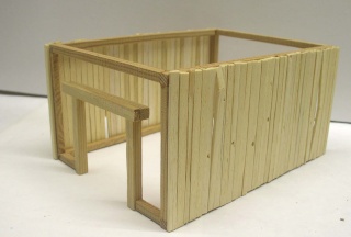 Structure en bois clair d'une grange médiévale miniature en cours d'assemblage avec ouverture latérale