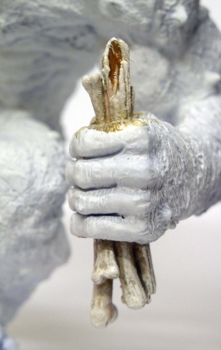 Gros plan de la main de la figurine en apprêt blanc serrant un bâton sculpté