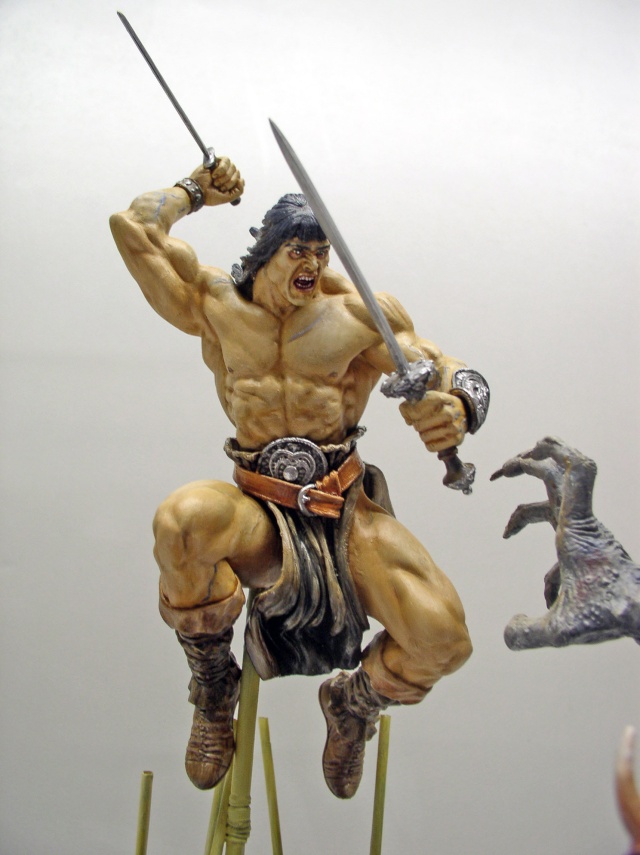 Figurine de Conan bondissant avec deux épées face à une créature griffue