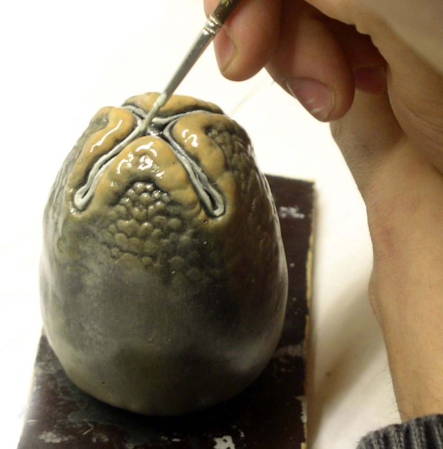Main appliquant au pinceau les détails peints sur la tête d'une figurine Alien
