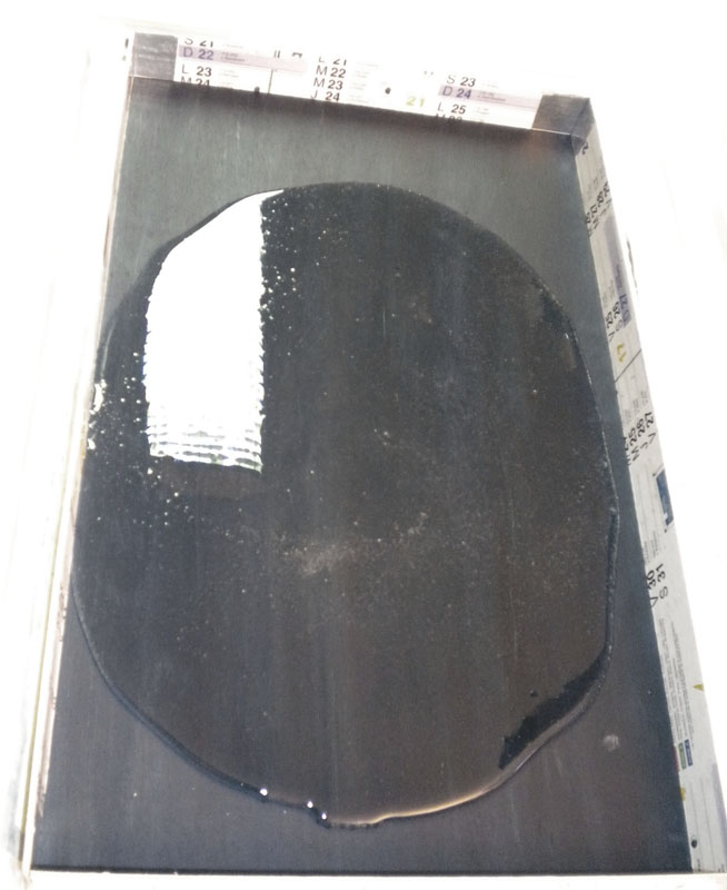 Flaque de résine noire en forme ovale coulée sur une plaque protégée par du papier journal