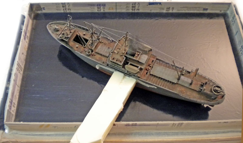 Maquette de cargo vieilli en cours de montage sur un diorama maritime gris