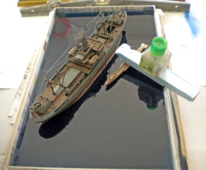 Maquette de Liberty ship vieillie posée sur un diorama de mer en cours de réalisation