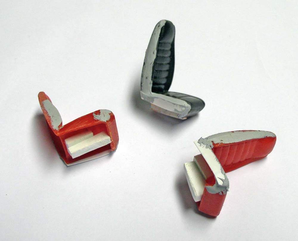 Trois sièges miniatures de maquette en cours de fabrication, peints en rouge et gris