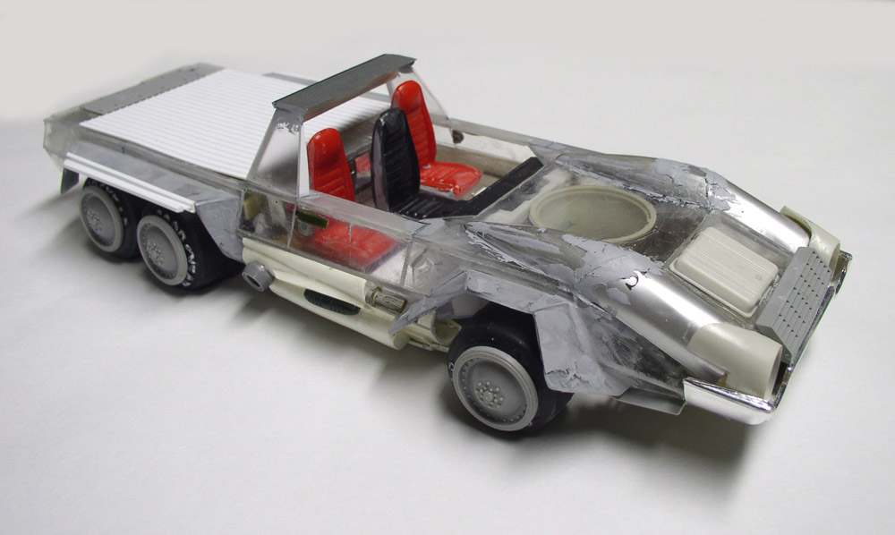 Maquette de véhicule futuriste à six roues avec sièges rouges et carrosserie métallisée