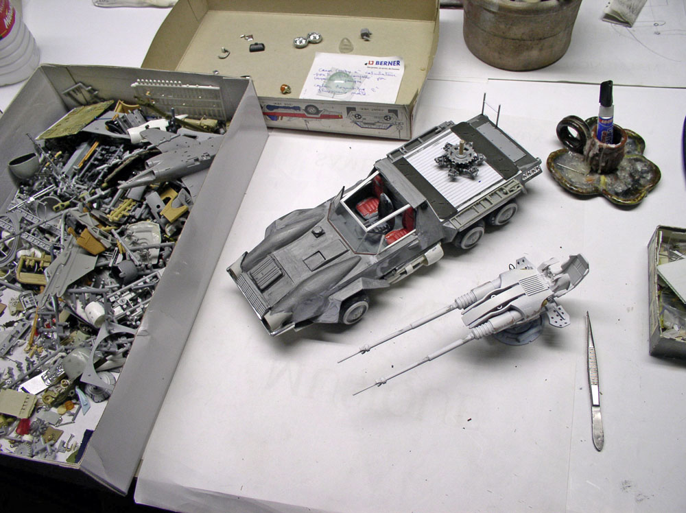 Maquettes d'un véhicule blindé et d'un vaisseau gris sur établi avec pièces détachées