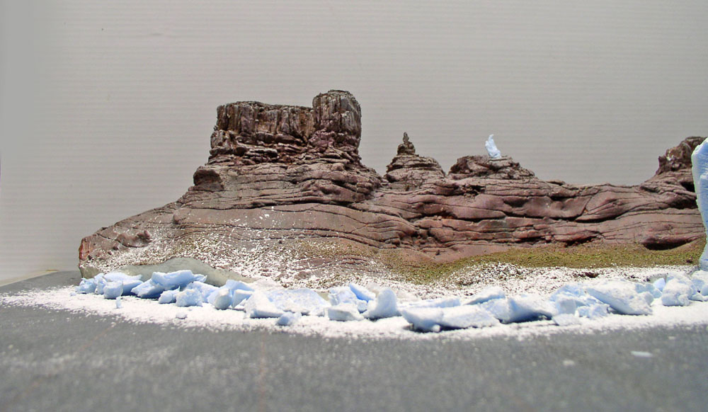 Diorama de maquette représentant des falaises rocheuses martiennes stratifiées bordées de glace bleutée et de neige