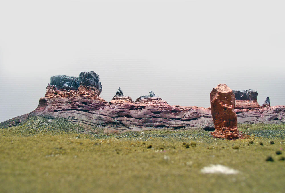 Maquette d'un paysage martien avec formations rocheuses rougeâtres stratifiées et sol verdâtre sous un ciel brumeux