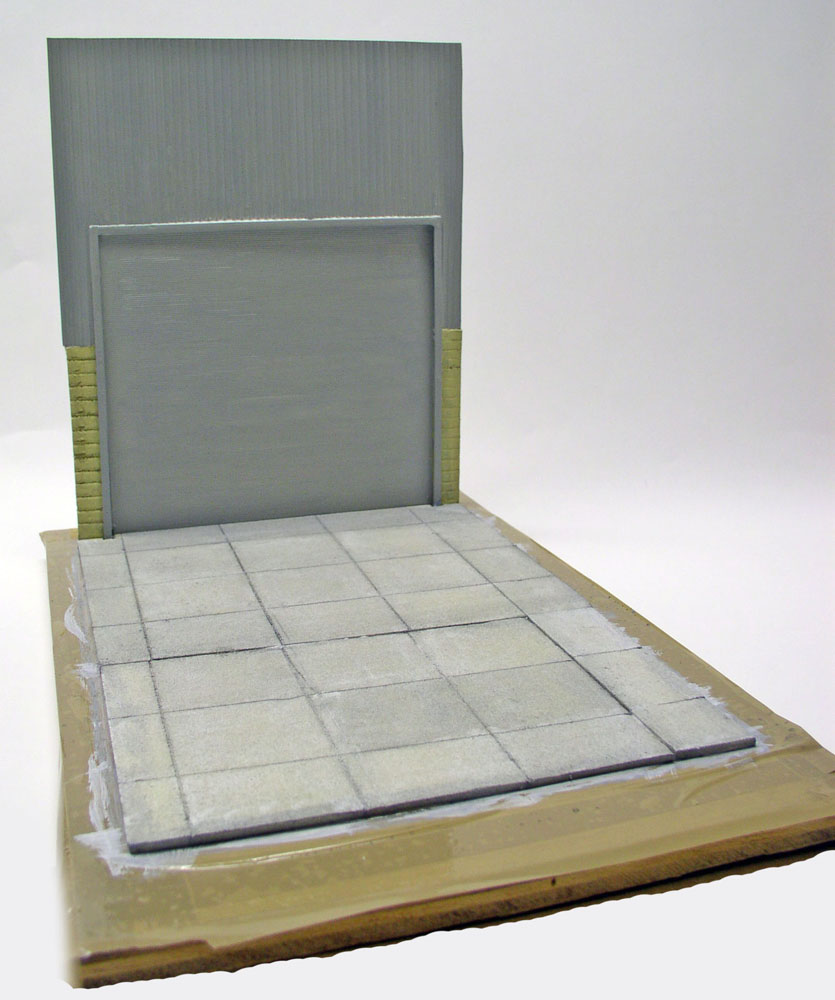 Diorama en construction avec mur gris et sol pavé en cours de peinture