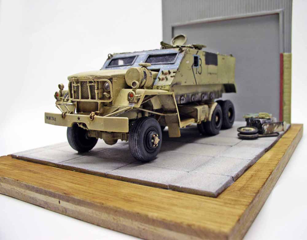 Maquette de guntruck blindé sable sur diorama de sol pavé devant un hangar