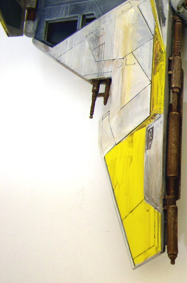 Détail de la maquette d'épave spatiale montrant un fuselage gris et jaune vieilli avec tuyauteries rouillées