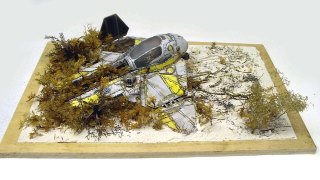 Maquette d'épave de vaisseau spatial jaune et gris échouée dans un diorama végétalisé