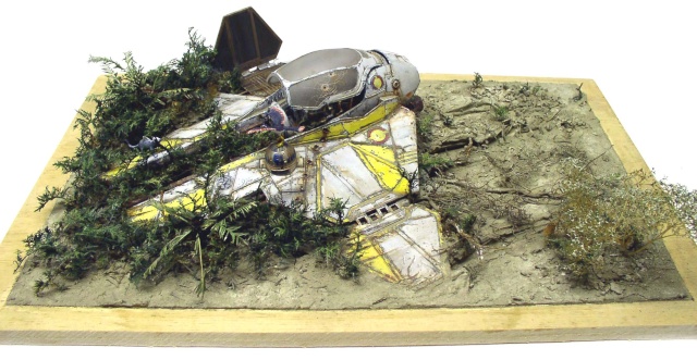 Maquette d'épave de vaisseau spatial jaune et blanc écrasé dans un diorama de végétation