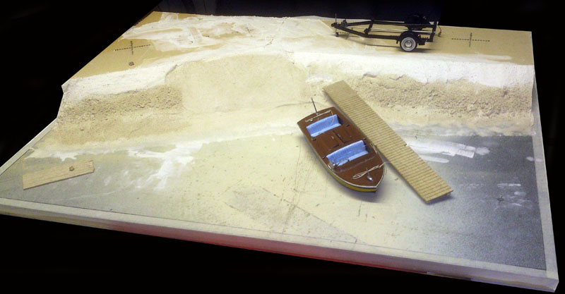 Diorama en cours avec maquette de bateau amarrée à un ponton et remorque sur la berge