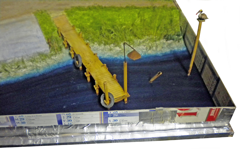 Diorama avec ponton en bois sur eau en résine bleue et berge herbeuse