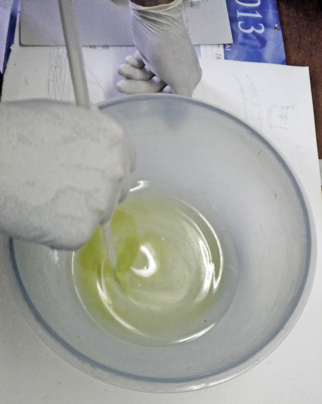 Mains gantées mélangeant la résine teintée en vert dans un bol en verre