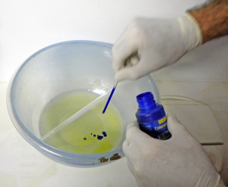 Mains gantées ajoutant du colorant bleu dans un bol de résine liquide