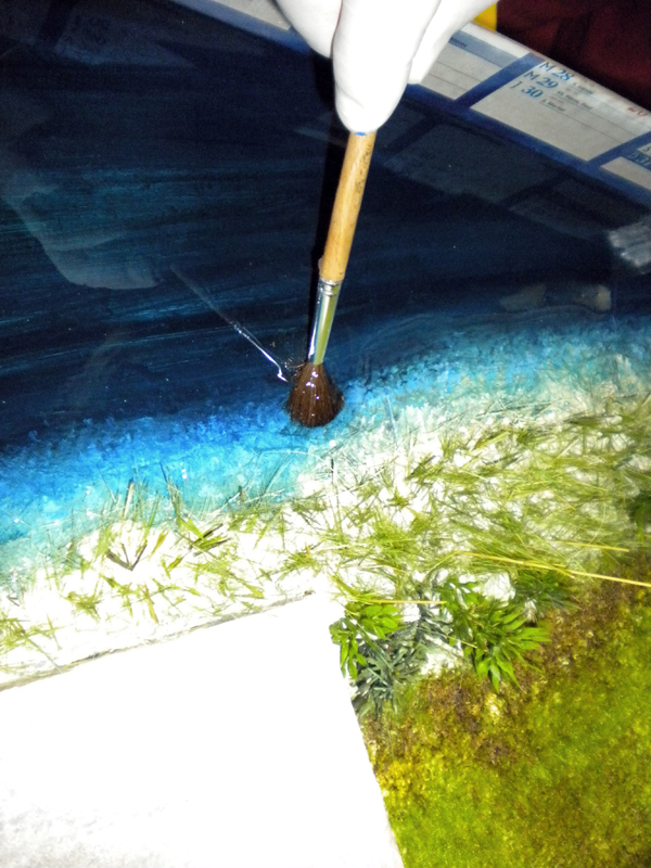 Application au pinceau de la texture d'écume sur l'eau en résine bleue d'un diorama