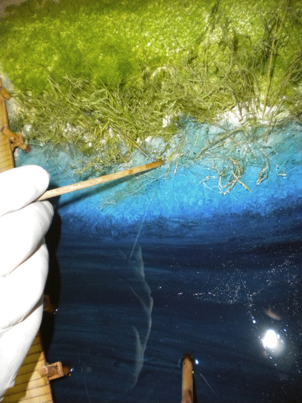 Application de résine bleue sur la berge herbeuse d'un diorama avec un cure-dent