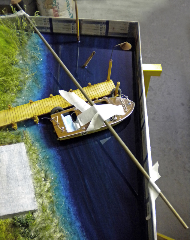 Diorama avec eau en résine bleue, barque en bois et ponton jaune près de la berge