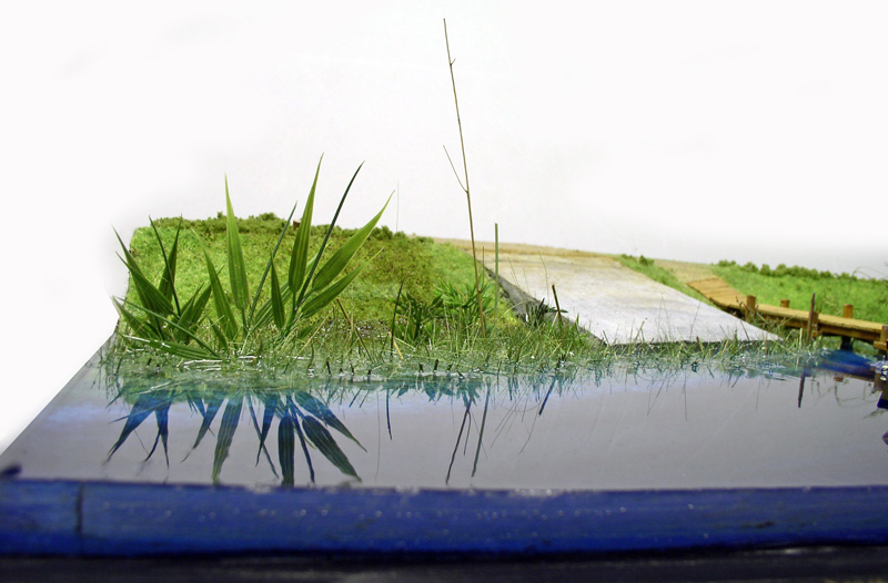 Plan d'eau en résine sur diorama avec touffes d'herbe et reflets sur la berge