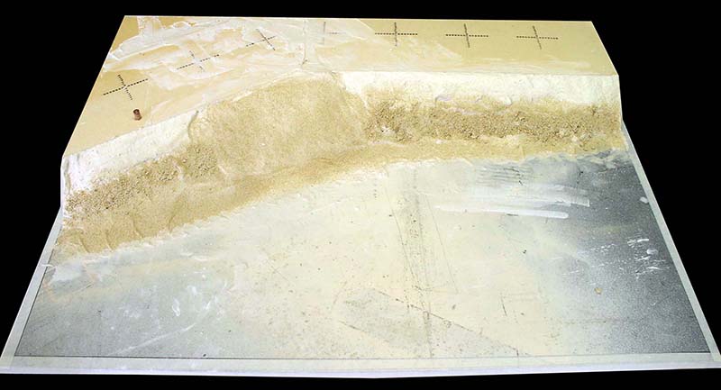 Diorama en construction avec berge de sable et surface plane préparée avant la coulée de résine