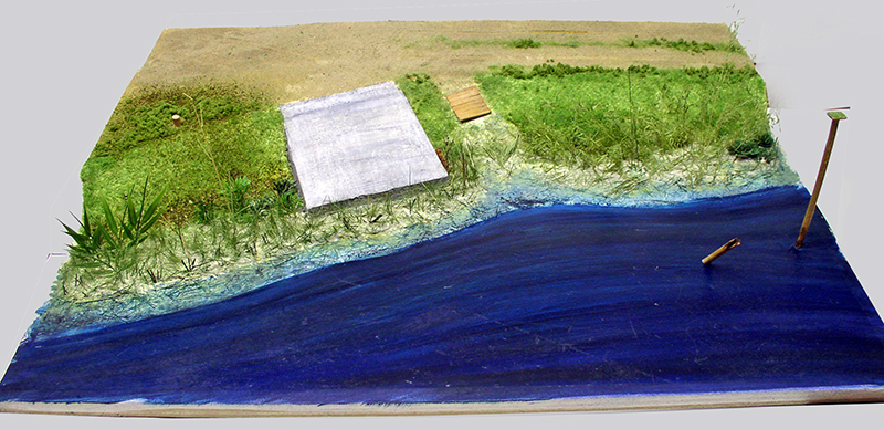 Diorama d'une berge herbeuse bordant un plan d'eau bleu en résine