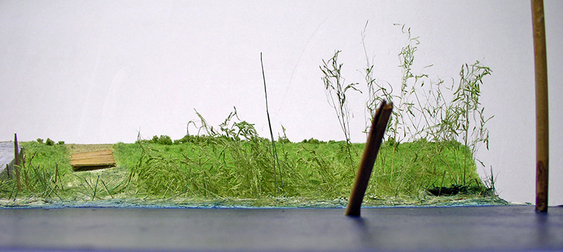 Berge de diorama avec herbes hautes et végétation surplombant une surface d'eau en résine