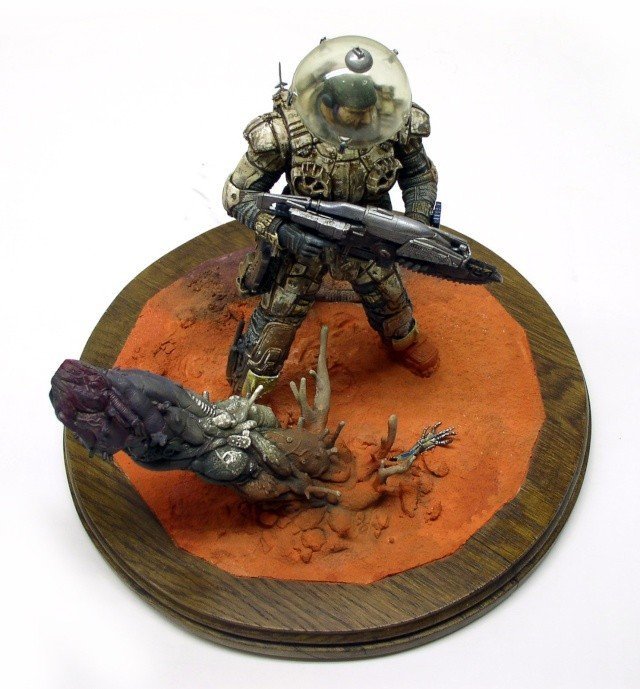 Figurine de Marcus Fenix avec casque et fusil face à une créature sur socle rond