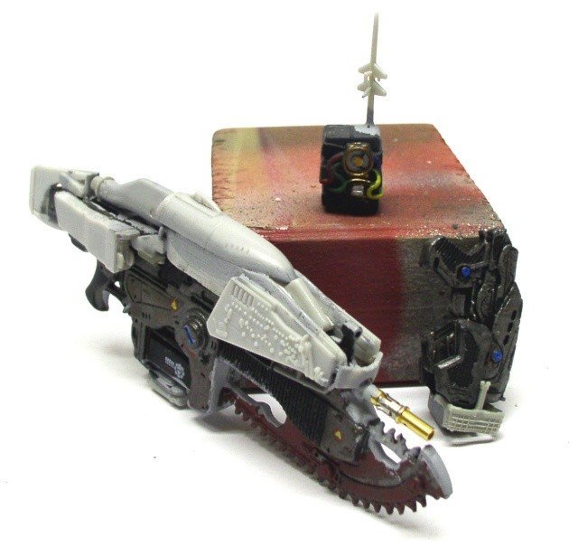 Maquette du fusil Lancer de Marcus Fenix en cours de peinture devant un socle rouge