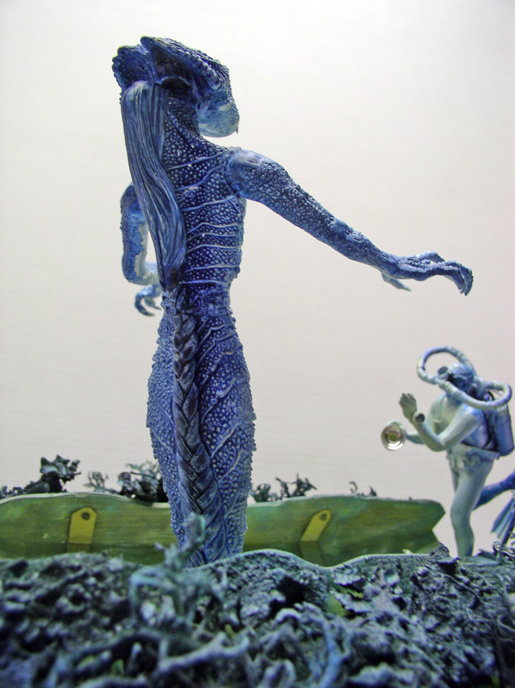 Figurine de démon marin bleu écaillé tendant le bras vers un plongeur sur fond marin