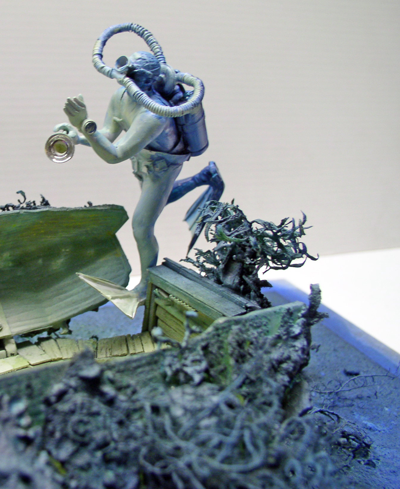 Figurine de plongeur tenant une lampe sur diorama d'épave marine envahie d'algues