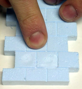 Doigts pressant des briques de polystyrène extrudé bleu découpées pour imiter un mur de pierre