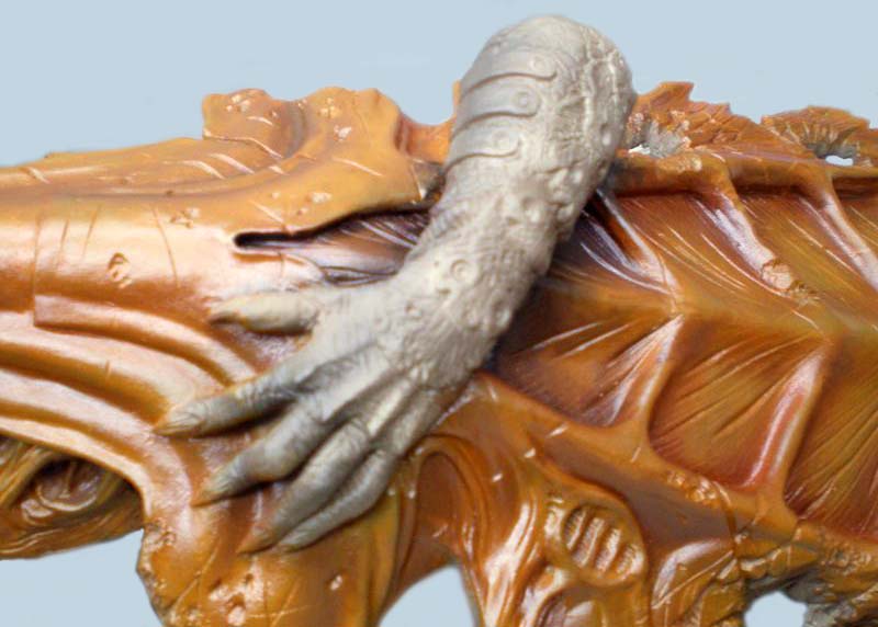 Gros plan d'une main grise de figurine Predator posée sur un corps musclé peint en ocre