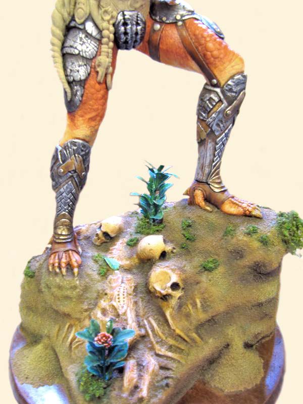 Jambes peintes de la figurine Predator sur un socle rocheux avec crânes et végétation