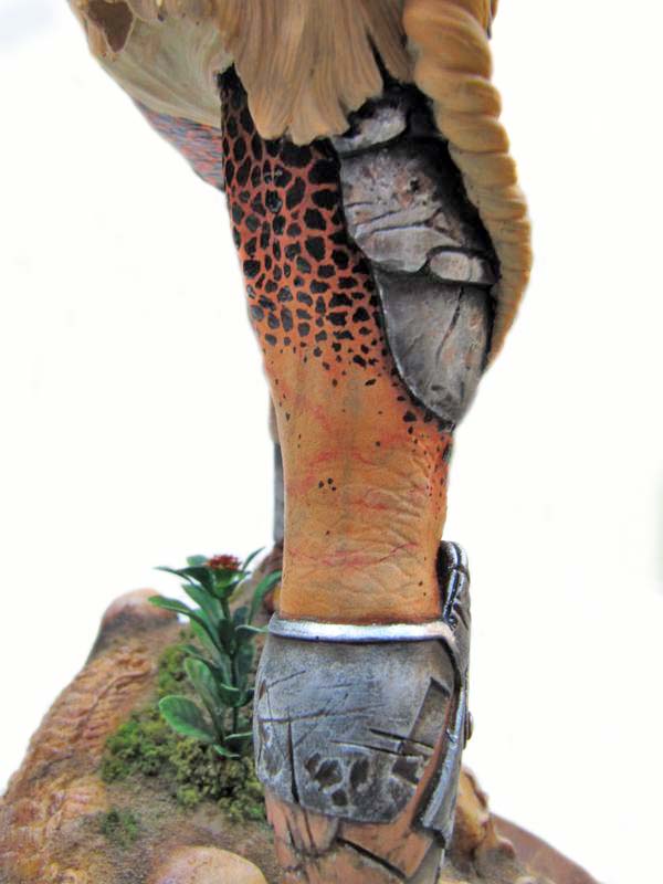 Détail de la jambe peinte du Predator avec armure métallique, sur socle rocheux fleuri