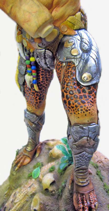 Détail des jambes écailleuses du Predator avec armures métalliques et perles colorées sur socle rocheux