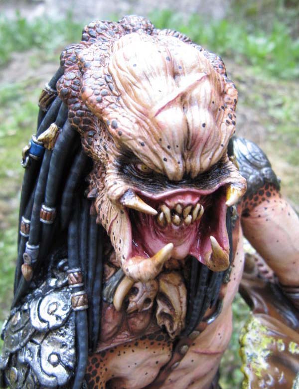 Gros plan de la figurine Predator gueule ouverte montrant crocs et mandibules, dreadlocks en extérieur