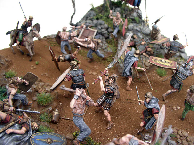 Diorama de figurines représentant une bataille entre légionnaires romains et guerriers barbares sur terrain rocheux