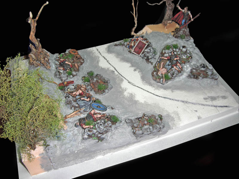 Diorama de scénette romaine avec figurines, sentier, rochers, arbres morts et végétation sur socle blanc