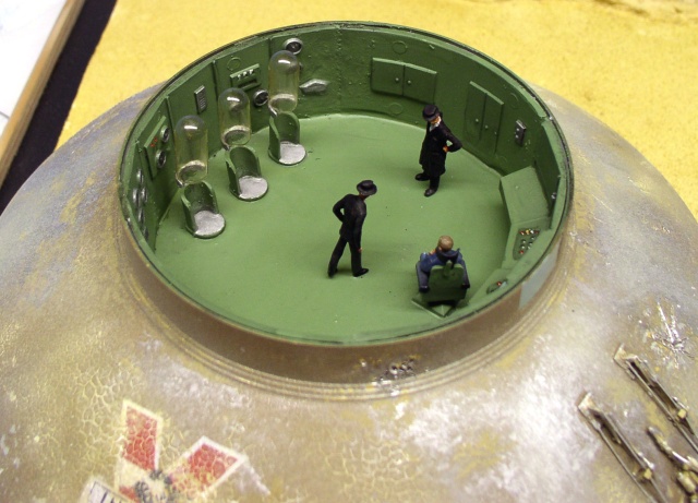 Intérieur vert de la soucoupe maquette avec trois figurines en uniforme et postes de pilotage