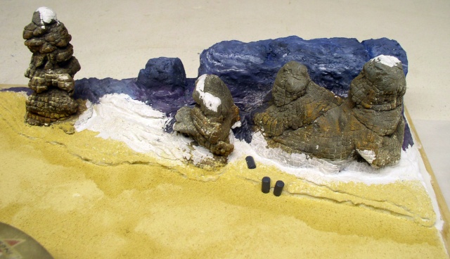 Diorama de maquettisme avec figurines rocheuses enneigées sur sable et falaise bleue