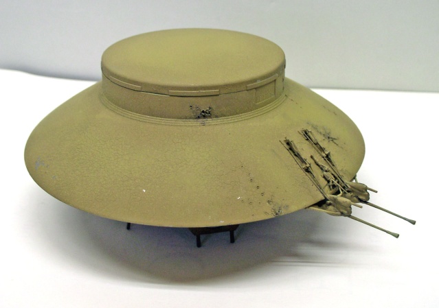 Maquette de soucoupe volante beige sur trépied, équipée de canons latéraux, sur fond blanc