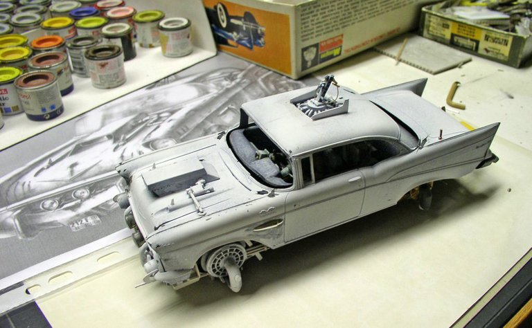 Maquette de Chevrolet 1957 en apprêt gris sur l'établi entouré de pots de peinture