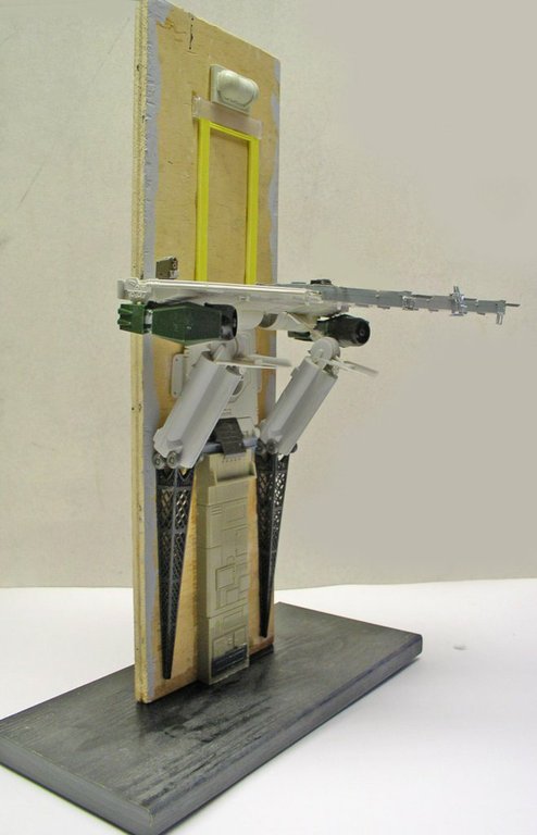 Maquette de robot bipède futuriste en construction monté sur socle gris devant panneau vertical